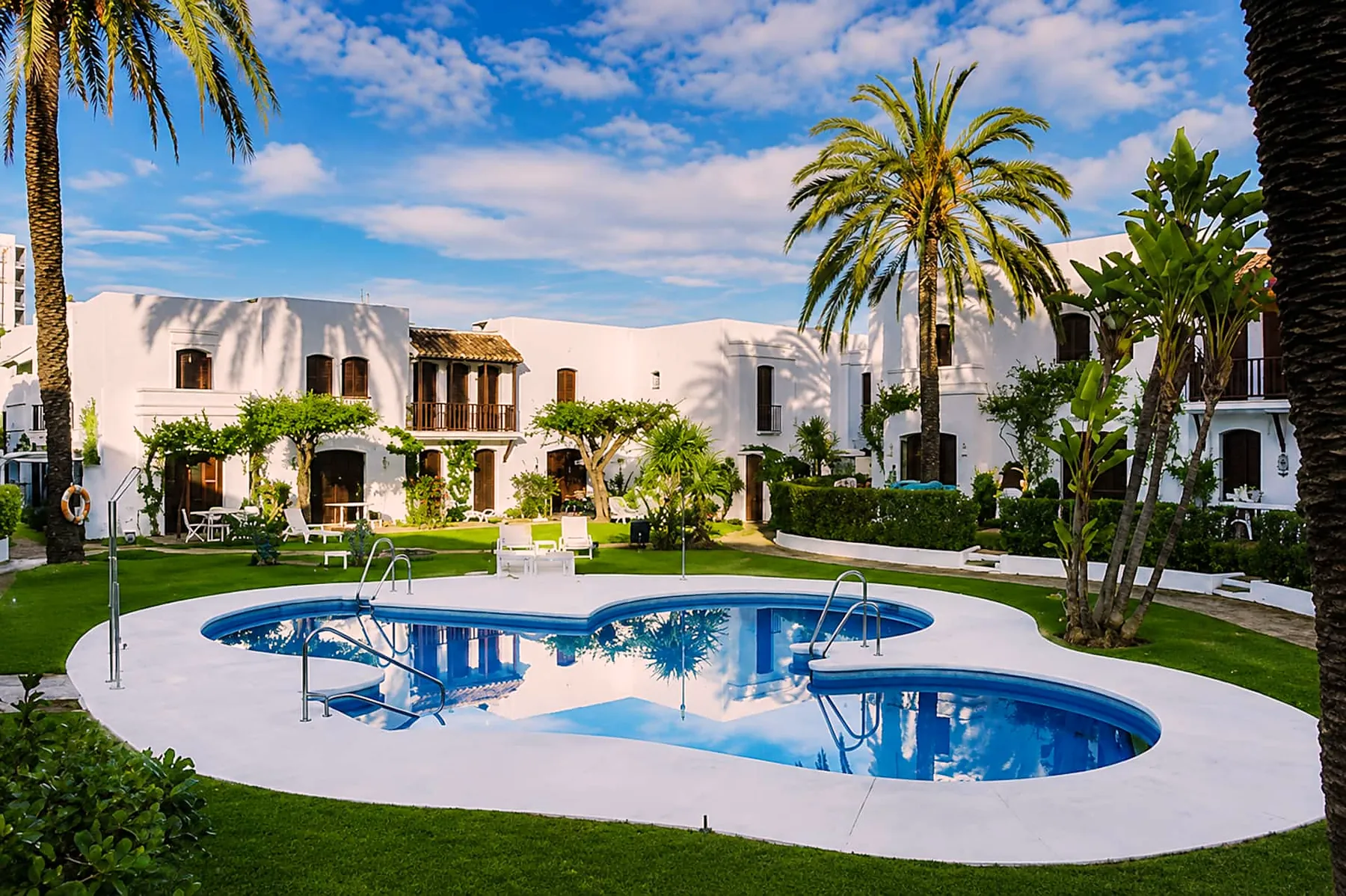 Resort pool among palm trees and whitewashed houses